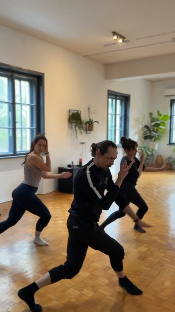 Roman leading a class in a sunlit ZEN Studio with wooden parquet floors, tall windows, and hanging plants