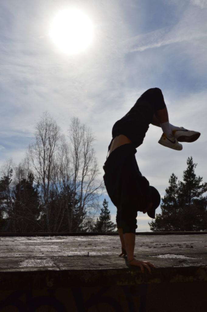 Silhouetted handstand against the sun on a rooftop, bare trees behind