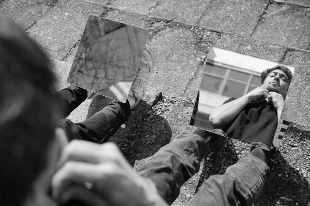 Two mirrored surfaces on pavement, reflecting portrait and sneaker