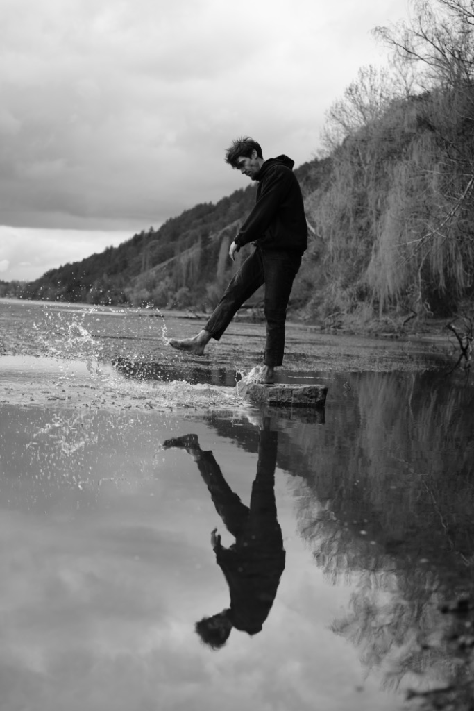 Roman stepping off a stone into a still lake, splash rising